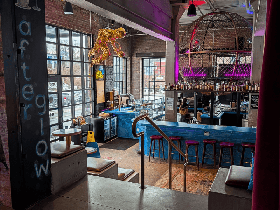 column with afterglow painted on with a blue bar in the background, a gold astronaut sculpture hanging from the ceiling and purple metal DJ globe shaped cage column with afterglow painted on with a blue bar in the background, a gold astronaut sculpture hanging from the ceiling and purple metal DJ globe shaped cage