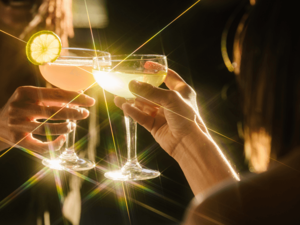 two people cheer with coop glasses cocktails and lots of golden hour lighting two people cheer with coop glasses cocktails and lots of golden hour lighting