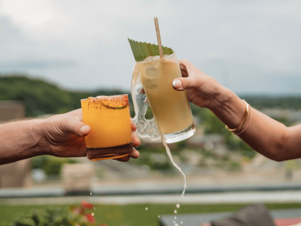 two people cheer drinks with one spilling their drink on a rooftop bar two people cheer drinks with one spilling their drink on a rooftop bar
