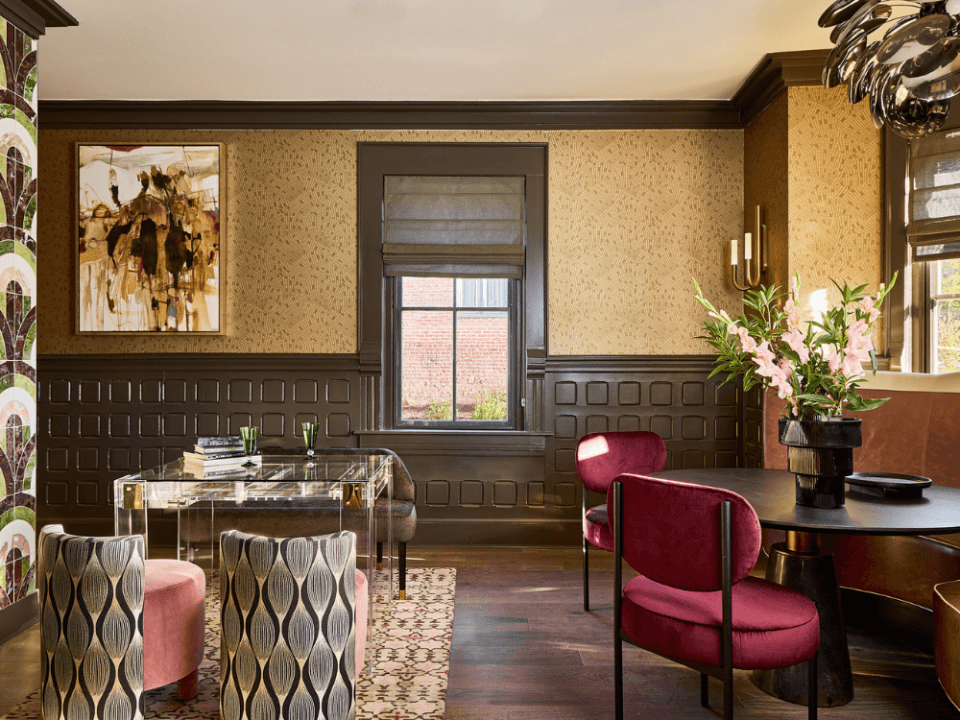Room with two seating areas, one with velvet maroon chairs around a brown wood circle table, and one with patterned black and white backs and pink seats around a glass table Room with two seating areas, one with velvet maroon chairs around a brown wood circle table, and one with patterned black and white backs and pink seats around a glass table