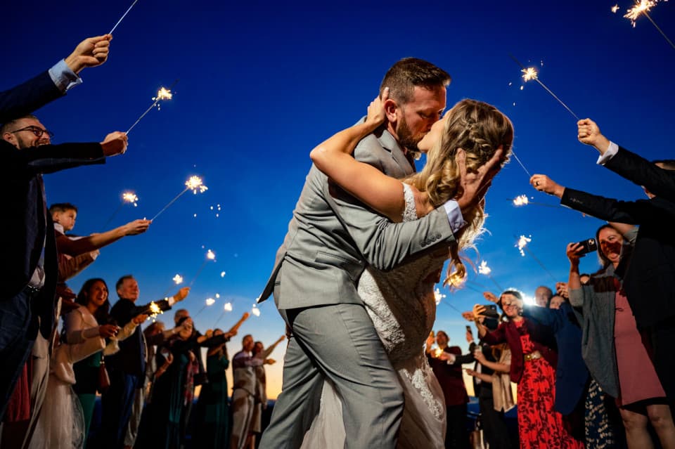 bride and groom kiss at a nc wedding while surrounded by wedding guests with sparklers during blue hour bride and groom kiss at a nc wedding while surrounded by wedding guests with sparklers during blue hour