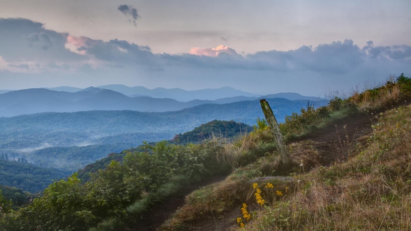 A view of rolling blue hills layered in the distance from a hiking trail in Asheville