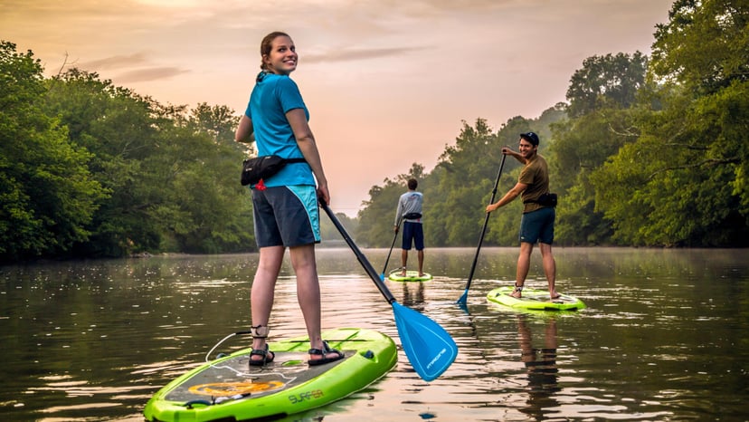 Three people paddle down an Asheville waterway at sunset
