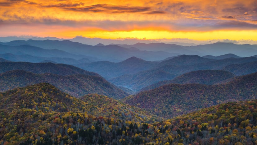 Blue mountains below a sun-streaked orange sky in Asheville
