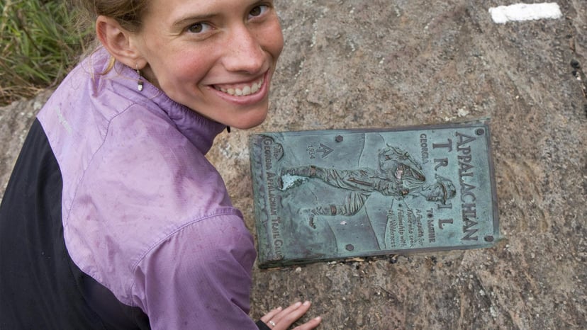 A hiker poses next to an Appalachian Trail plaque