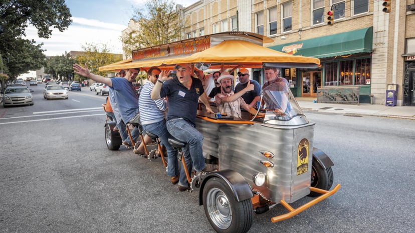 A group of people laugh as they pedal on a moving bar on a beer tour in Asheville