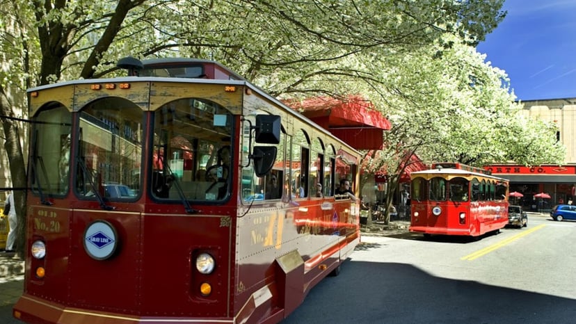 a trolly bus is parked on a charming street with green trees in Asheville