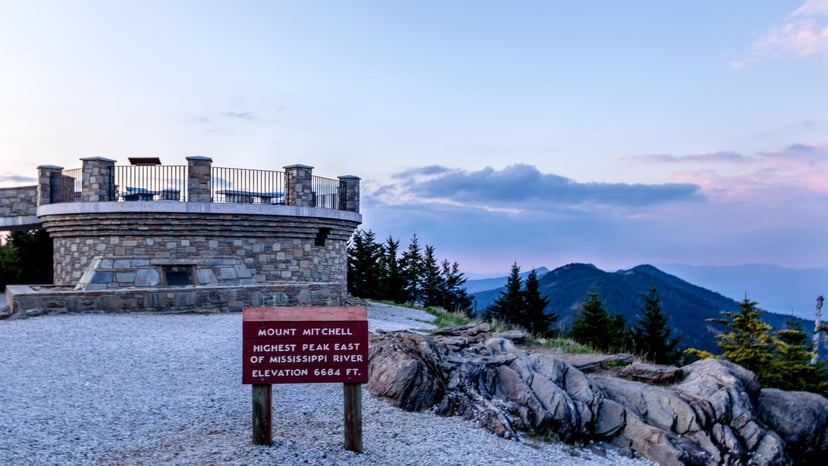 a sign read "Mt. Mitchell" at sunset, overlooking beautiful mountains
