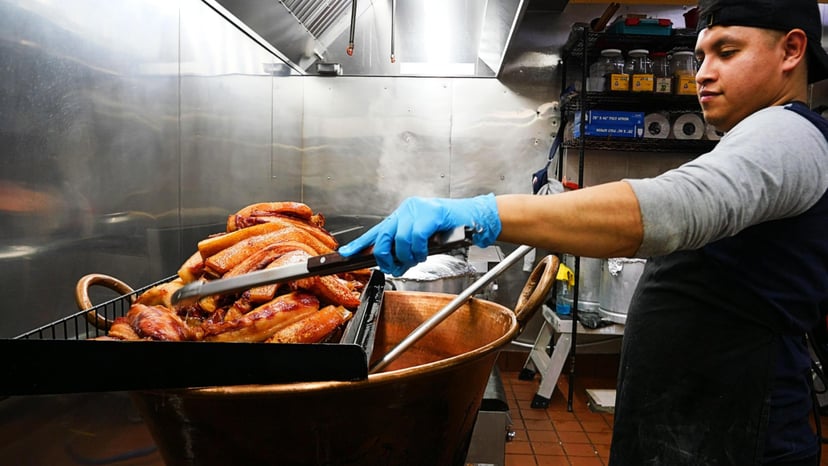 A chef cooks pork over a large copper vat