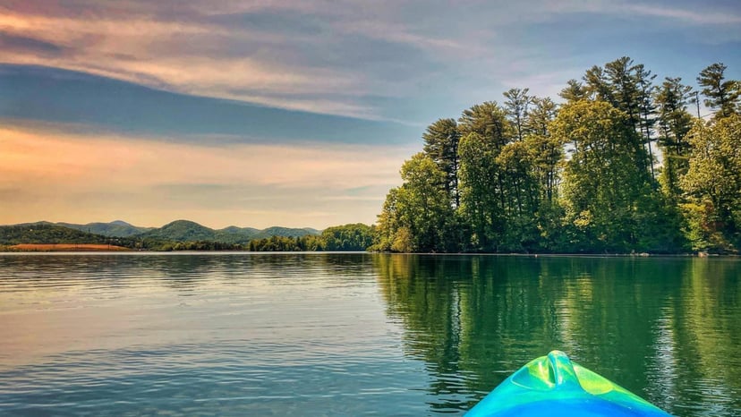a kayak floats on a lake looking at a shore at sunset