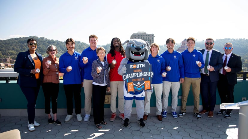 Leaders from the Big South Conference, Explore Asheville, UNC Asheville, USC Upstate, and Gardner-Webb pose with student-athletes and UNC Asheville mascot at the press conference announcing that McCormick Field will host the Big South Baseball Championship in 2026 and 2027.